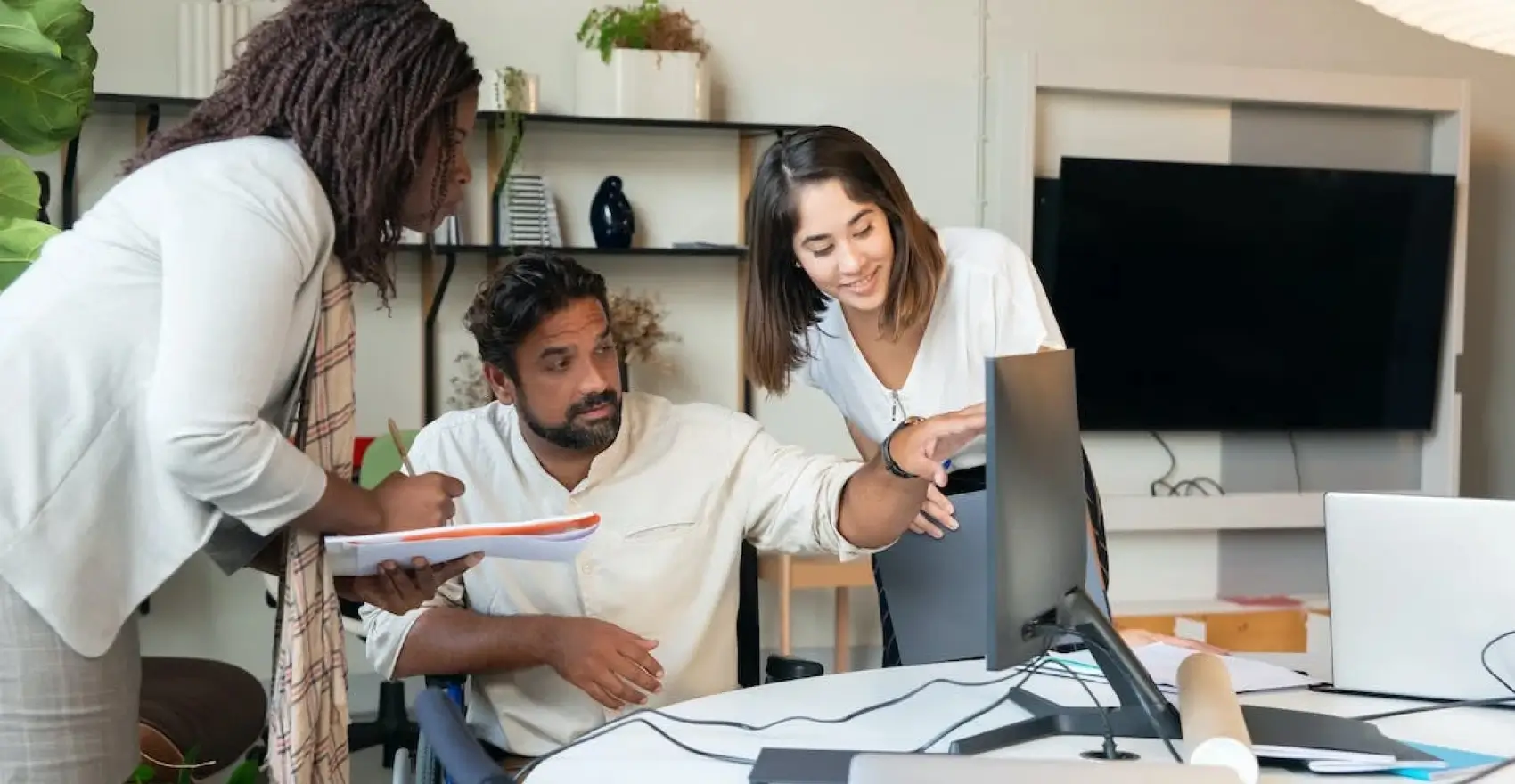 Three professionals collaborating in an office setting, discussing a project while reviewing a computer screen, emphasizing teamwork and communication in staffing solutions.
